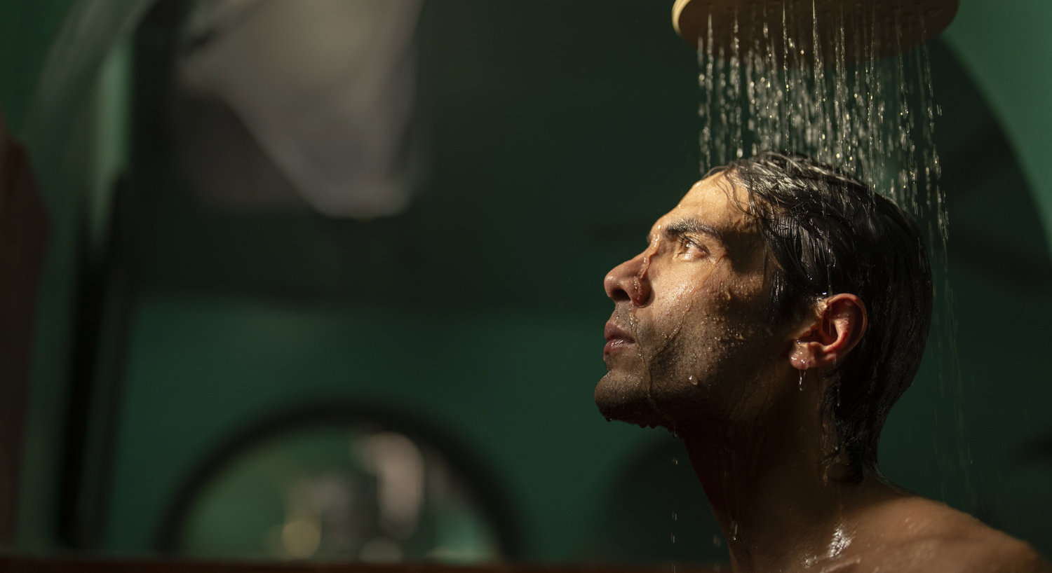 Man standing underneath round shower head with water falling on his head