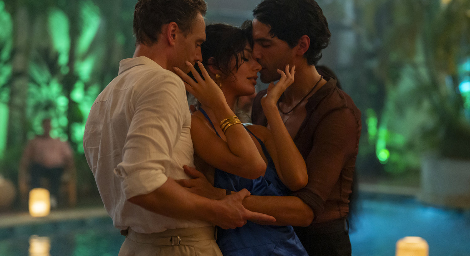 Woman in blue dress standing between two men with her hands on their faces