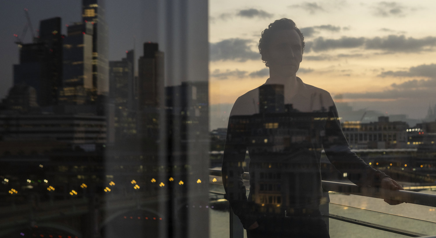 Man standing on balcony with reflection of city in background
